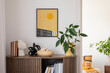 © FollowTheFlow - Stylish interior with a wooden cabinet adorned with potted plants, decorative objects, and books. A vibrant art piece featuring a sunburst design adds a pop of color. Cozy seating area.