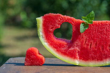 Fresh juicy red watermelon slice with heart shape hole on nature background in outdoors garden in summer time, closeup. Concept of happiness, love, holidays and vacation