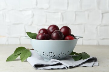 Wall Mural - Ripe plums in colander and leaves on light textured table