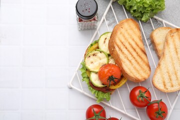 Tasty sandwich with grilled vegetables and fresh ones on white tiled table, flat lay. Space for text