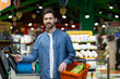 © Liubomir - Man at grocery store using self-checkout machine, holding credit card, paying for groceries. Shopper has basket filled with fresh vegetables. Bright store environment emphasizes convenient