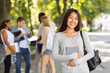 © Prostock-studio - Happy asian girl student holding notepad and smiling at camera, spending time with friends in public park