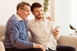 © Prostock-studio - Mature Son Teaching Senior Father To Use Mobile Phone Sitting On Sofa Indoor. Selective Focus