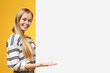 © Prostock-studio - Look here. Beautiful teenage girl pointing at white blank placard with open palm, orange background