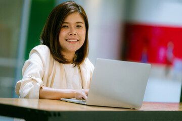 Smiling professional young Asian businesswoman talking in front of the camera having video conference with her business partners on laptop in a contemporary office space