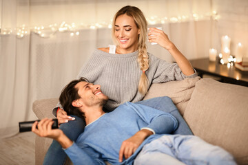 Wall Mural - Young couple enjoying winter holidays, talking and watching tv on sofa in cozy room