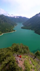 Wall Mural - Plansee Austria, At this viewpoint, you can see a tranquil lake nestled among lush green mountains under a clear blue sky. A couple of man and woman on top of an mountain