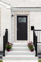 Wall Mural - A front door detail on a white brick home with concrete steps and black railing leading to a black front door with a mosaic window.