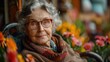 © Elena - Elderly woman wearing glasses sitting in chair with flowers in background