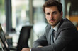 © StockUp - Young professional man in a suit sits at a desk in a modern office space, looking into the camera confidently.