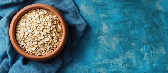 Poster - Oat flakes in a clay bowl on a blue linen napkin Dry rolled oats on wooden boards Healthy eating idea. with copy space image. Place for adding text or design