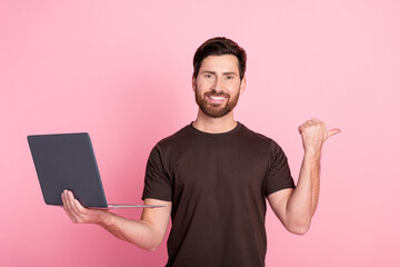 Poster - Photo of optimistic nice guy dressed brown t-shirt holding laptop indicating at discount empty space isolated on pink color background