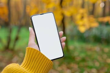 Woman holding a smartphone with a blank white screen for a mockup in an outdoor park