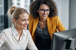 © polack - Woman Boss helping woman employee at her workplace on computer, they smile. They look at computer screen together in bright office