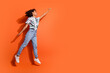 © deagreez - Full body photo of woman in jeans and summer stylish shirt jumping trampoline raised fist up superhero isolated on orange color background