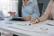 © amnaj - Businesswomen analyzing financial data and pointing at charts on a desk in the office