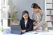 © amnaj - Two young businesswomen are analyzing financial data on a digital tablet, collaborating on a project in a modern office