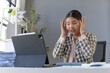 © amnaj - Businesswoman is holding her head with her hands, suffering from a headache while working on a challenging task using a digital tablet in the office