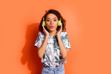 Wall Mural - Photo portrait of brown wavy haired girl wear summer shirt listen audio playlist in wireless headphones pouted lips isolated on orange color background