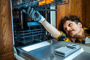 Latino man fixing dishwasher in the kitchen.