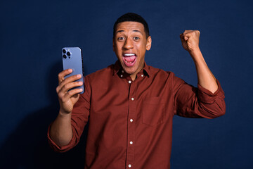 Poster - Photo of funky lucky guy dressed brown shirt winning game modern device emtpy space isolated blue color background