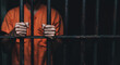 © K KStock - Man in orange prison issued clothing holding on to prison bars