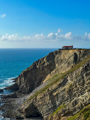 Rocky ocean coast on a sunny day, lighthouse standing on the edge. Faro de Cabo Vidio.