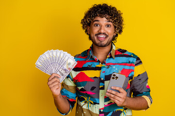 Wall Mural - Photo portrait of pretty young guy hold money fan gadget wear trendy colorful outfit isolated on yellow color background