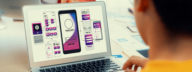 Panorama banner of startup UX developer or company employee design user interface or UI prototype for mobile application or website software with software display on laptop monitor in office. Synergic