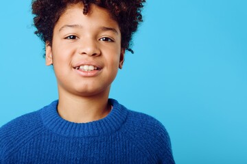 smiling african american boy with curly hair posing against a vibrant blue background in casual attire