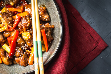 Wall Mural - Pork in sweet and sour sauce with pineapple, capsicum, ginger in a bowl on a gray background. Copyspace. Close-up.