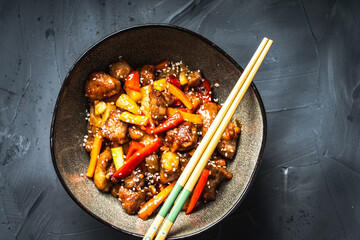 Wall Mural - Pork in sweet and sour sauce with pineapple, capsicum, ginger in a bowl on a gray background. Copyspace. Close-up.