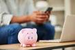 © Flashizzle/peopleimages.com - Piggy bank, person and phone for saving in home, investment and banking website for finance plan. Money jar, container and cashback for income growth, insurance fund and future security on table