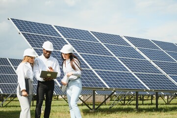 Wall Mural - Group of multi ethnic people and safety helmets staring at solar farm.