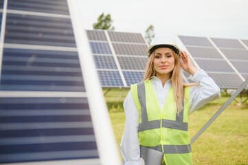 Wall Mural - Portrait of young female engineer standing near solar panels. Beautiful female professional in white helmet