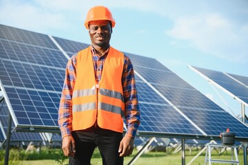 Wall Mural - African american man in safety helmet on solar panels with screwdriver. Competent technician using tools while performing service work on station