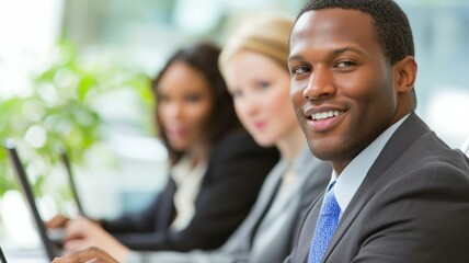 Three people in business attire are smiling and sitting at a table with laptops