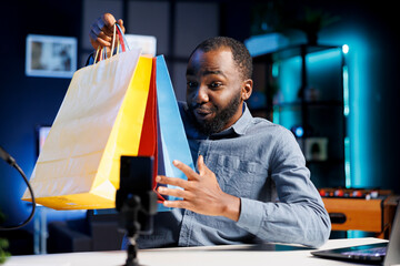 Wall Mural - BIPOC content creator filming video, unboxing bags with internet delivery order, showing subscribers purchases he recently got. Fashion designer presenting fans shopping acquisitions