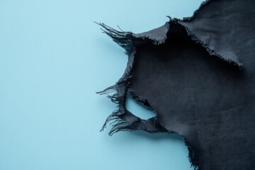 A closeup reveals a hole with frayed edges in black fabric, set against a soft pastel background, showcasing texture and material details