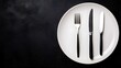 © Paul - Overhead shot of a white plate with neatly aligned fork and knife, black background, strong contrast created by focused studio lighting, extensive copy space.