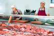 © JackF - In organic natural meat store, friendly farmer male seller stands near counter refrigerator display case. In butcher shop, elderly male vendor in uniform apron, gloves, cap holds cutting board