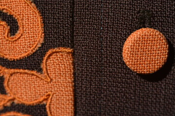 Orange button covered with material and orange ornament on woolen fabric close-up