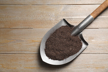 Wall Mural - Metal shovel with soil on wooden table, top view. Space for text