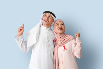 Wall Mural - Beautiful Muslim couple with red ribbons pointing at something on blue background. AID awareness concept