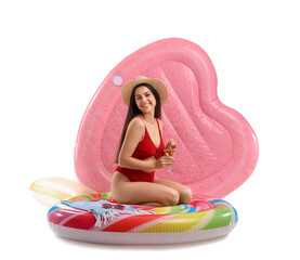 Wall Mural - Smiling young woman in swimsuit with cocktail and inflatable mattresses sitting on white background