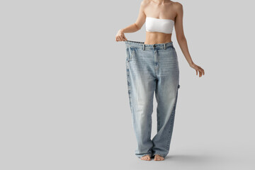 Canvas Print - Beautiful young sporty woman in loose jeans on grey background, closeup. Weight loss concept