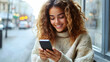 © Siasart Stock - A young woman smiles while using her smartphone in a cozy setting.