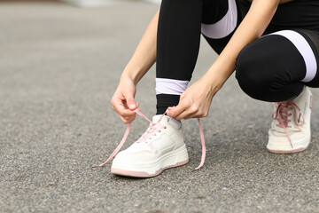 Wall Mural - Young woman in sportswear and stylish sneakers tying shoe laces outdoors, closeup