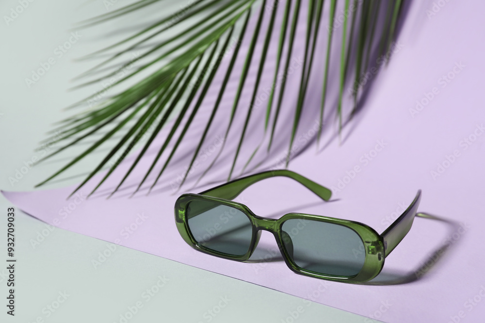 Stylish green sunglasses and palm leaf on colorful background