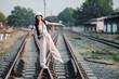 © Satori Studio - A young woman in casual clothing balances on railway tracks, holding a camera, symbolizing adventure and travel.